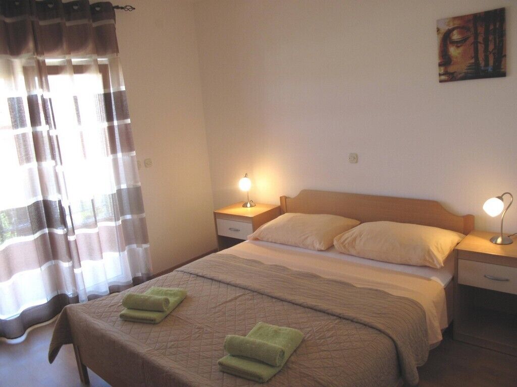 A neatly made bed with a quilt, two bedside lamps, a nightstand, and a window with curtains.