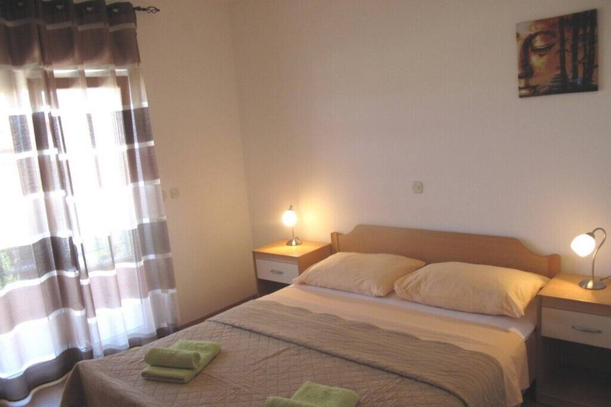 A neatly made bed with a quilt, two bedside lamps, a nightstand, and a window with curtains.