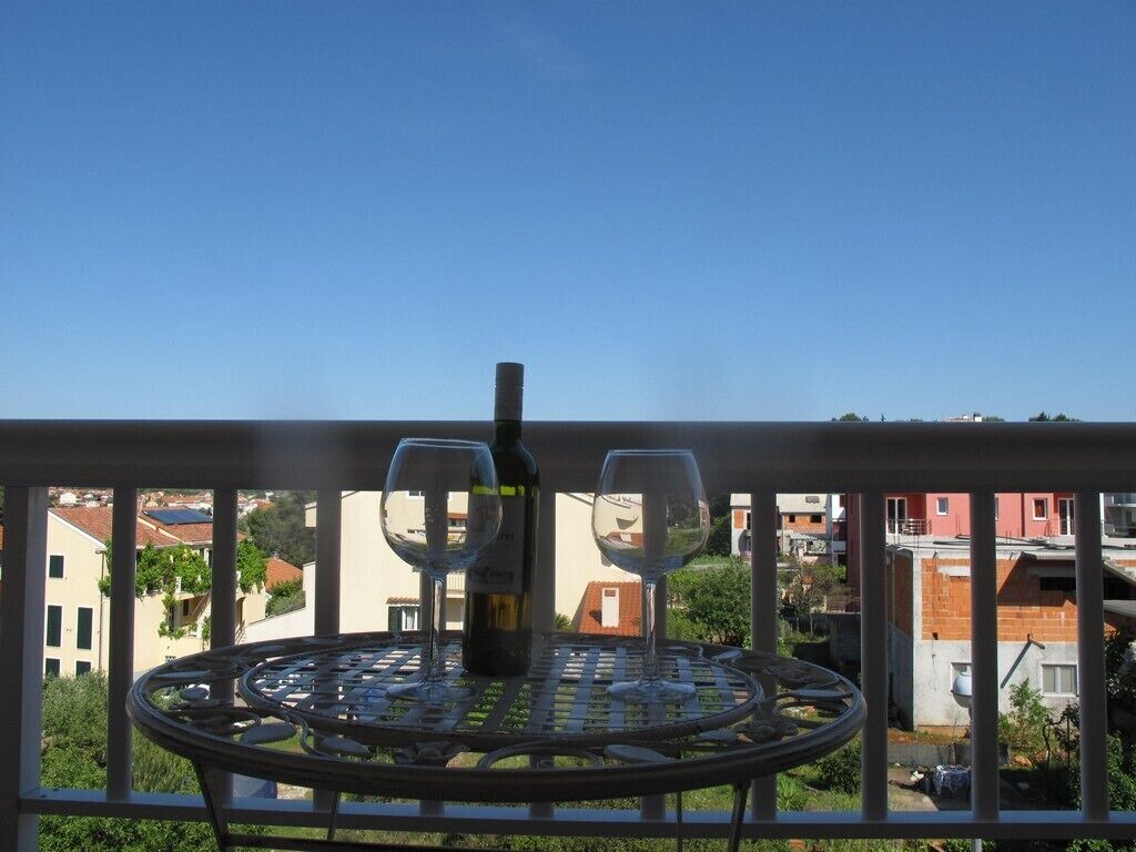 A balcony with a metal table, two chairs, a wine bottle, and a glass.
