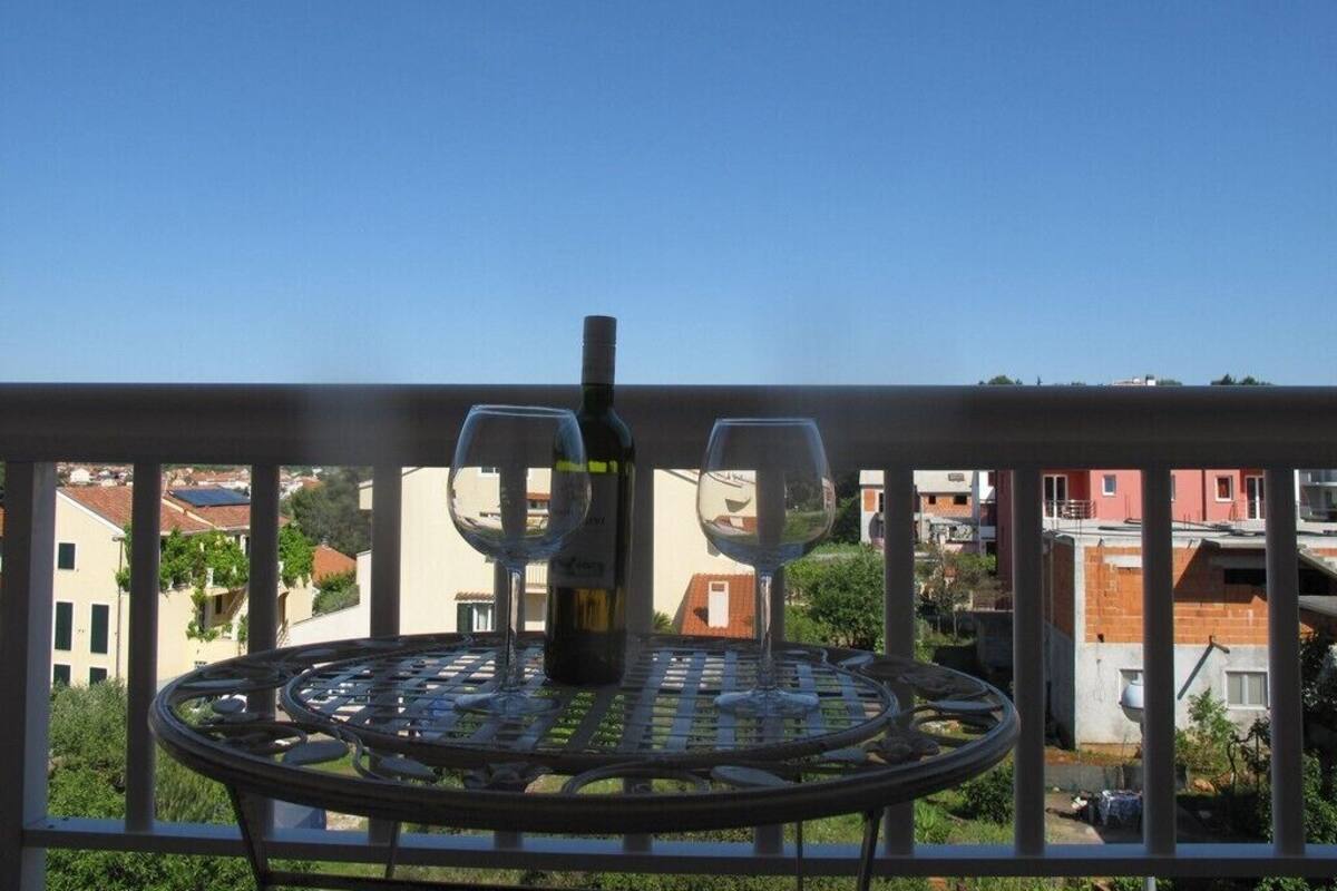 A balcony with a metal table, two chairs, a wine bottle, and a glass.