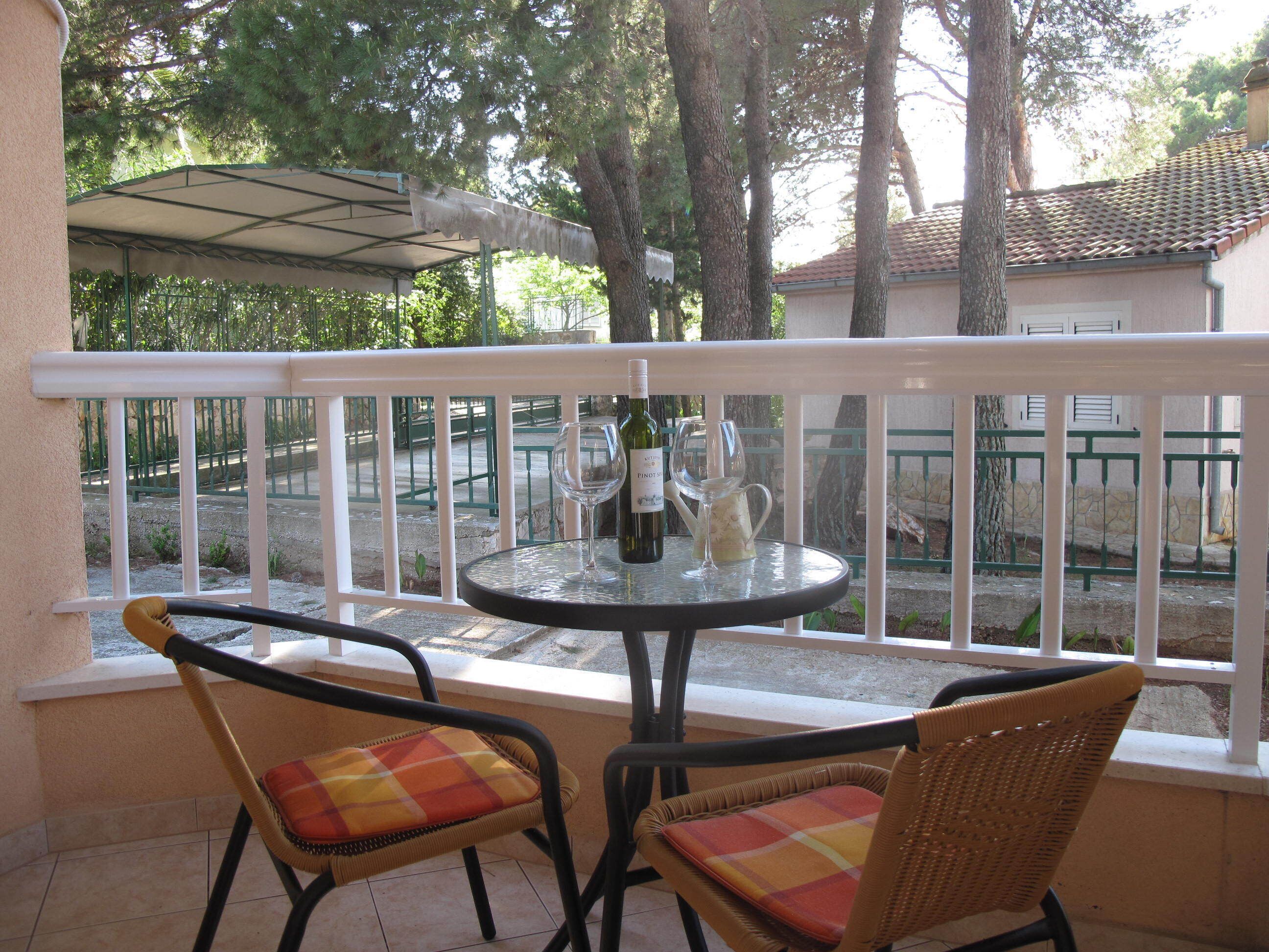 A balcony with a table and two wicker chairs, a bottle of wine, and a pitcher.