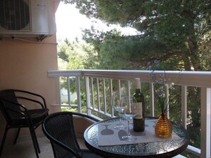 A balcony with a table, chairs, a bottle of wine, and a vase with flowers.