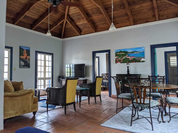 A spacious living room with a high wooden ceiling, a dining area with a table and chairs, and a sofa.