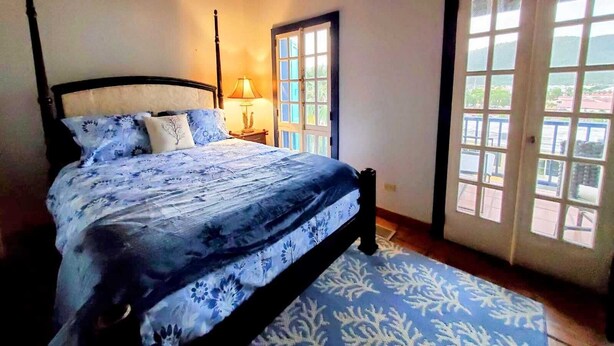 Un dormitorio con cama, mesita de noche, lámpara y vistas a través de una puerta.