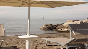 A beach with a white umbrella, two lounge chairs, and a sailboat in the distance. - Hotel Terme Oriente Beach & SPA (Ischia)