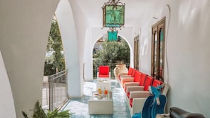 A narrow corridor with a tiled floor, a row of red and beige sofas, a blue scooter, and a hanging light fixture. - Hotel Terme Oriente Beach & SPA (Ischia)