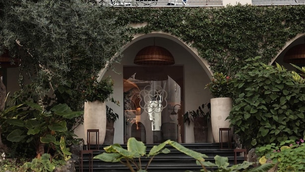 A building entrance with a covered staircase, surrounded by lush greenery and potted plants. - Hotel Terme Oriente Beach & SPA (Ischia)