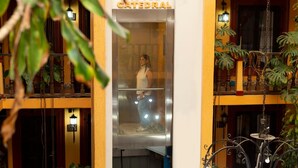 A hotel entrance with a glass elevator, a sign reading "HENVENO HOTEL CATEDRAL," and a balcony with plants and a wrought iron railing. - Catedral Hotel (San Cristóbal de las Casas)
