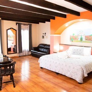 A hotel room with a bed, a leather sofa, a dining table with chairs, a mirror, and a painting on the wall. - Catedral Hotel (San Cristóbal de las Casas)