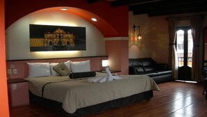 A hotel room with a bed, a black leather sofa, a painting on the wall, and a window with curtains. - Catedral Hotel (San Cristóbal de las Casas)