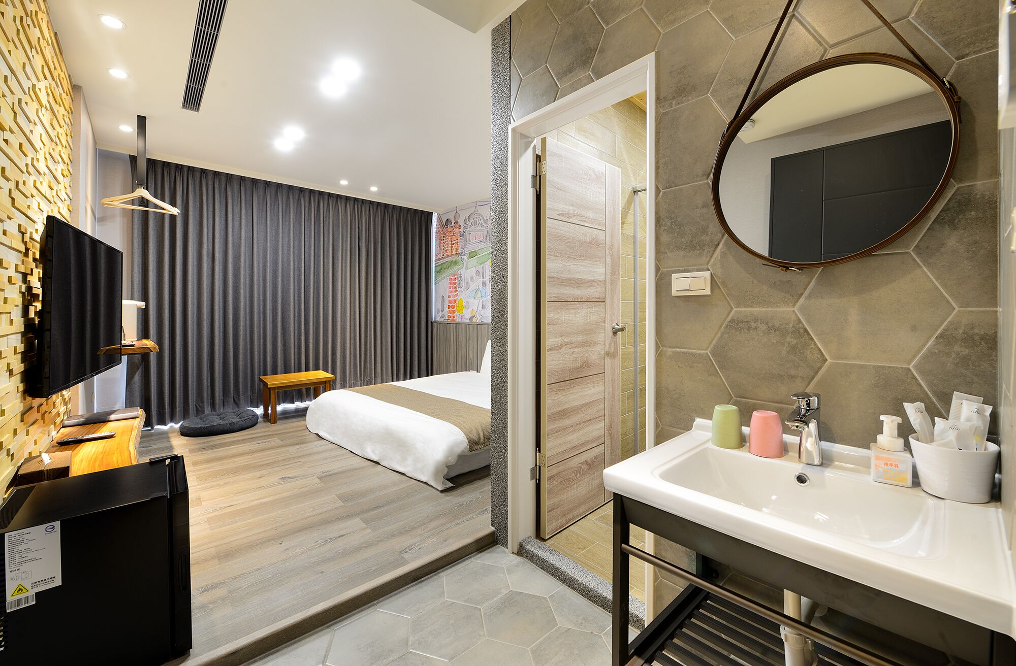 A modern hotel room with a large bed, a TV, a desk, and a bathroom with a sink and mirror.