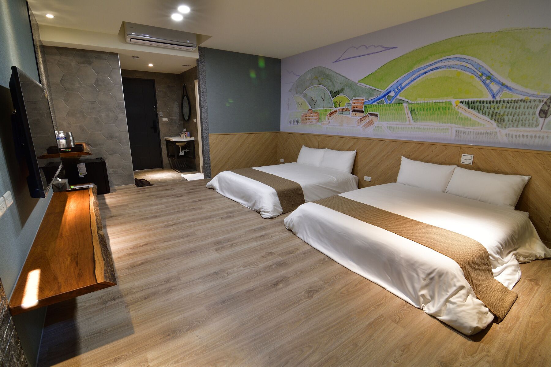 A hotel room with two beds, a wooden bench, a small bathroom, and a mural of a bridge.