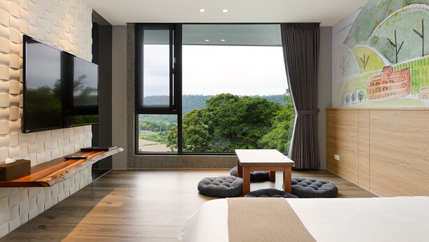 Un dormitorio moderno con un televisor grande, una mesa de madera y vistas a zonas verdes.