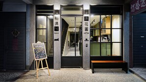 Entrada de un albergue, con un cartel que indica que es un hostel, un letrero de bienvenida y una banca en el exterior.