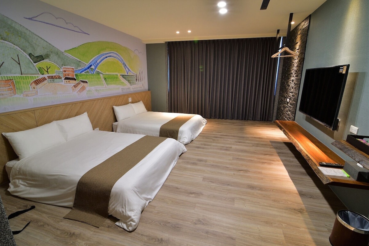 A hotel room with two beds, a mural on the wall, a flat-screen TV, and a wooden bench.