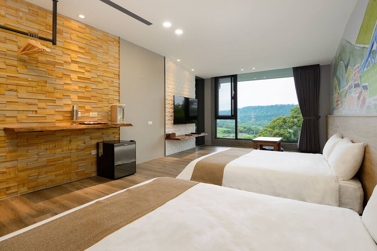 A modern hotel room with two beds, a wooden wall, a flat-screen TV, a coffee machine, and a view of the outdoors.