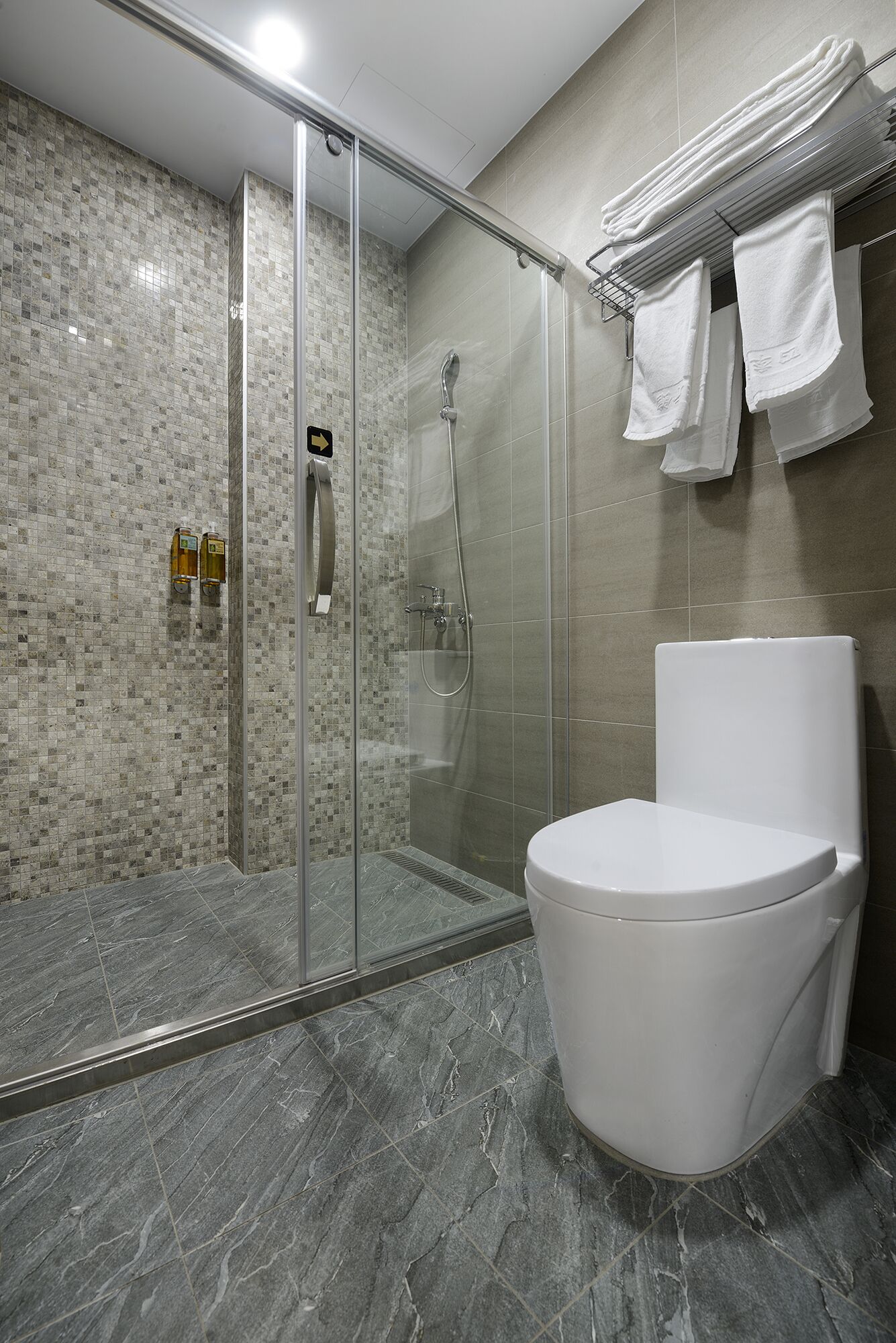 A modern bathroom with a glass-enclosed shower, a white toilet, and a towel rack with towels.