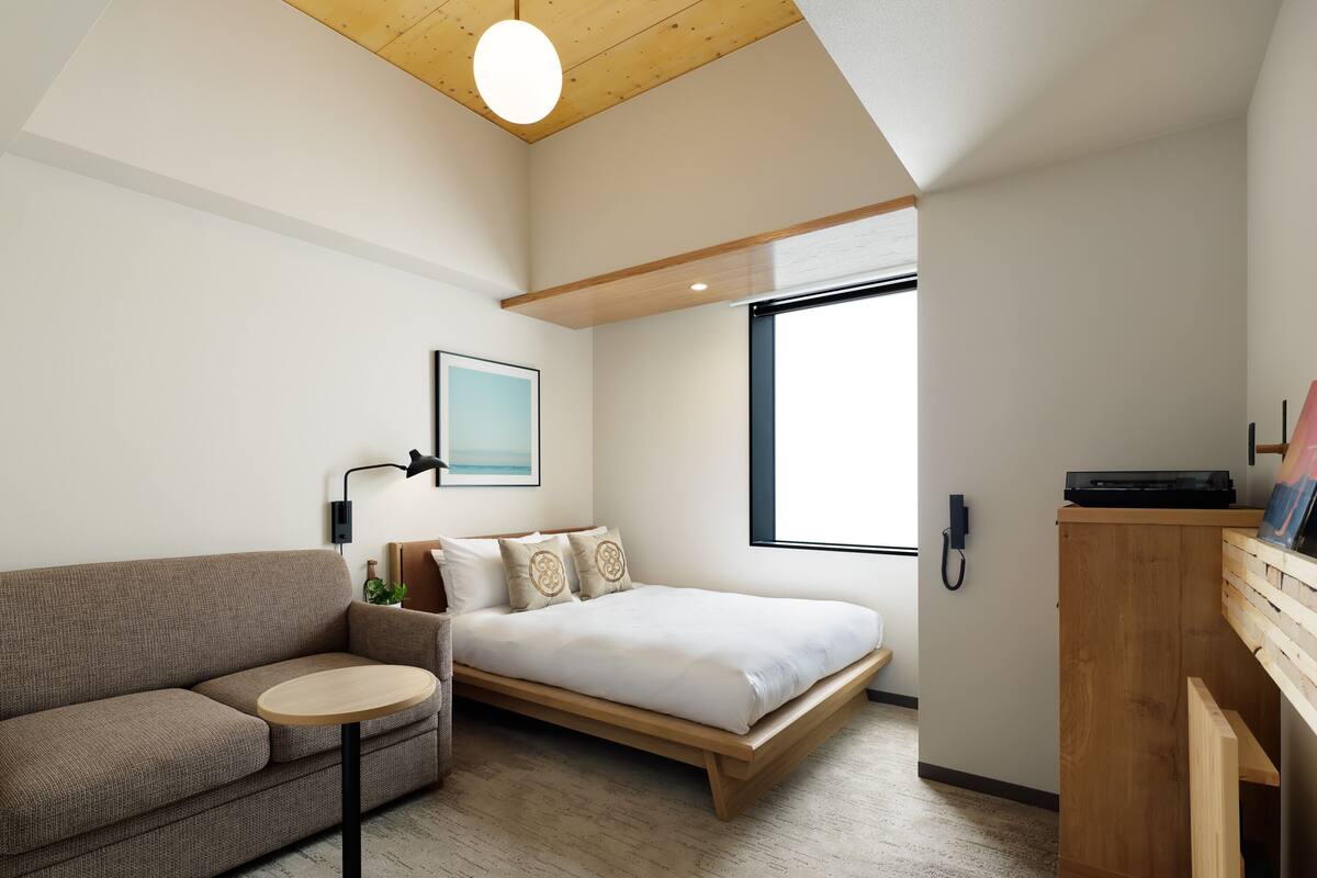 Un dormitorio moderno con cama tipo altillo, un sofá, una mesita y un armario de madera.