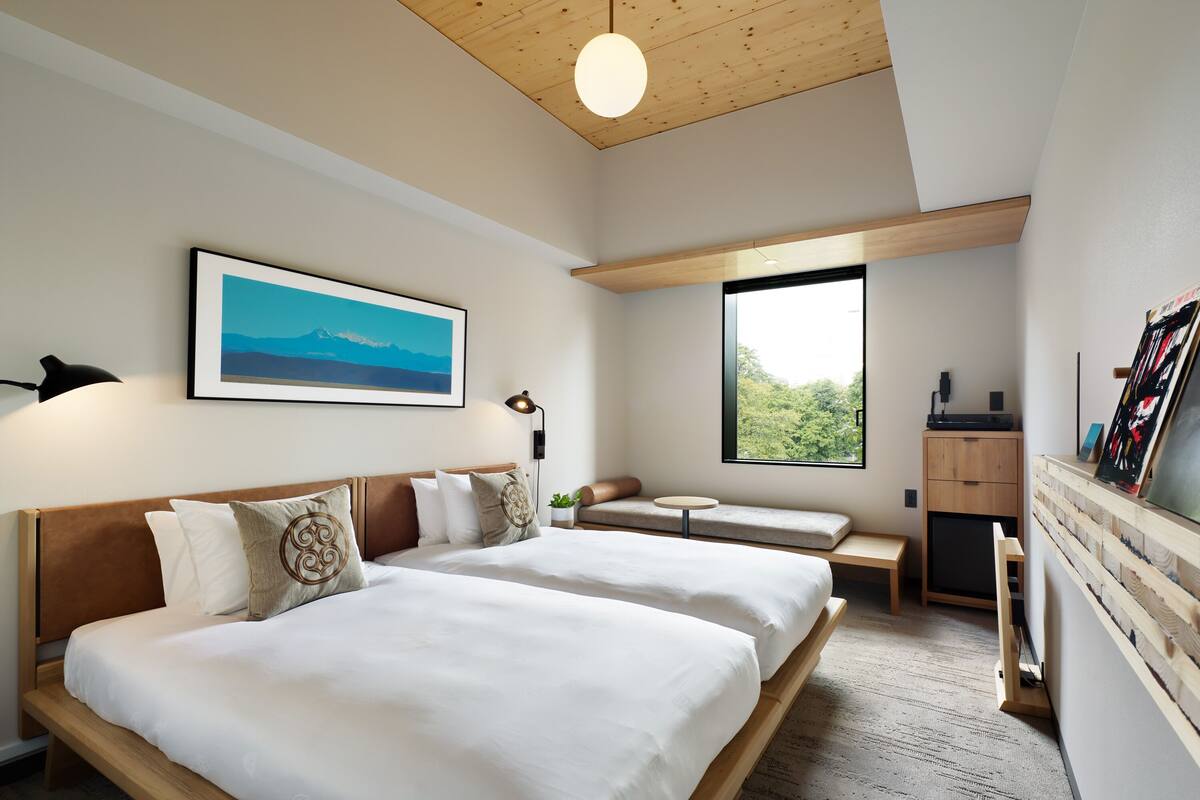 Una habitación de hotel moderna con dos camas, un ventanal grande, un escritorio y un cuadro en la pared.