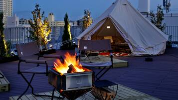 A rooftop terrace with a campfire, outdoor seating, and a tent.