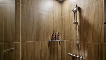 A shower area with a handheld showerhead, a wall-mounted shelf with toiletries, and a corner tile design.