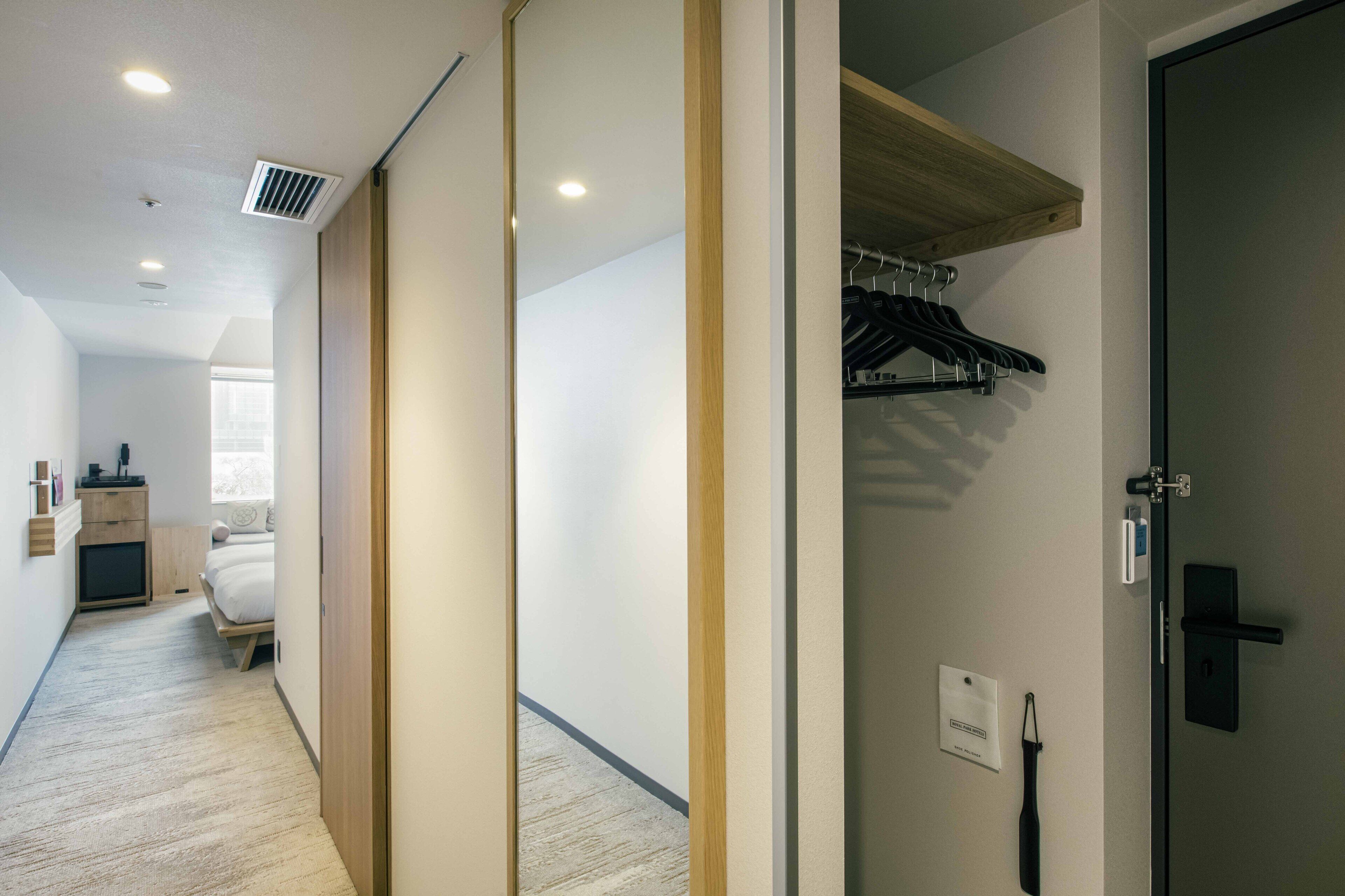 A hotel room with a bed, a bedside table, a wardrobe, and a closet with hanging clothes.