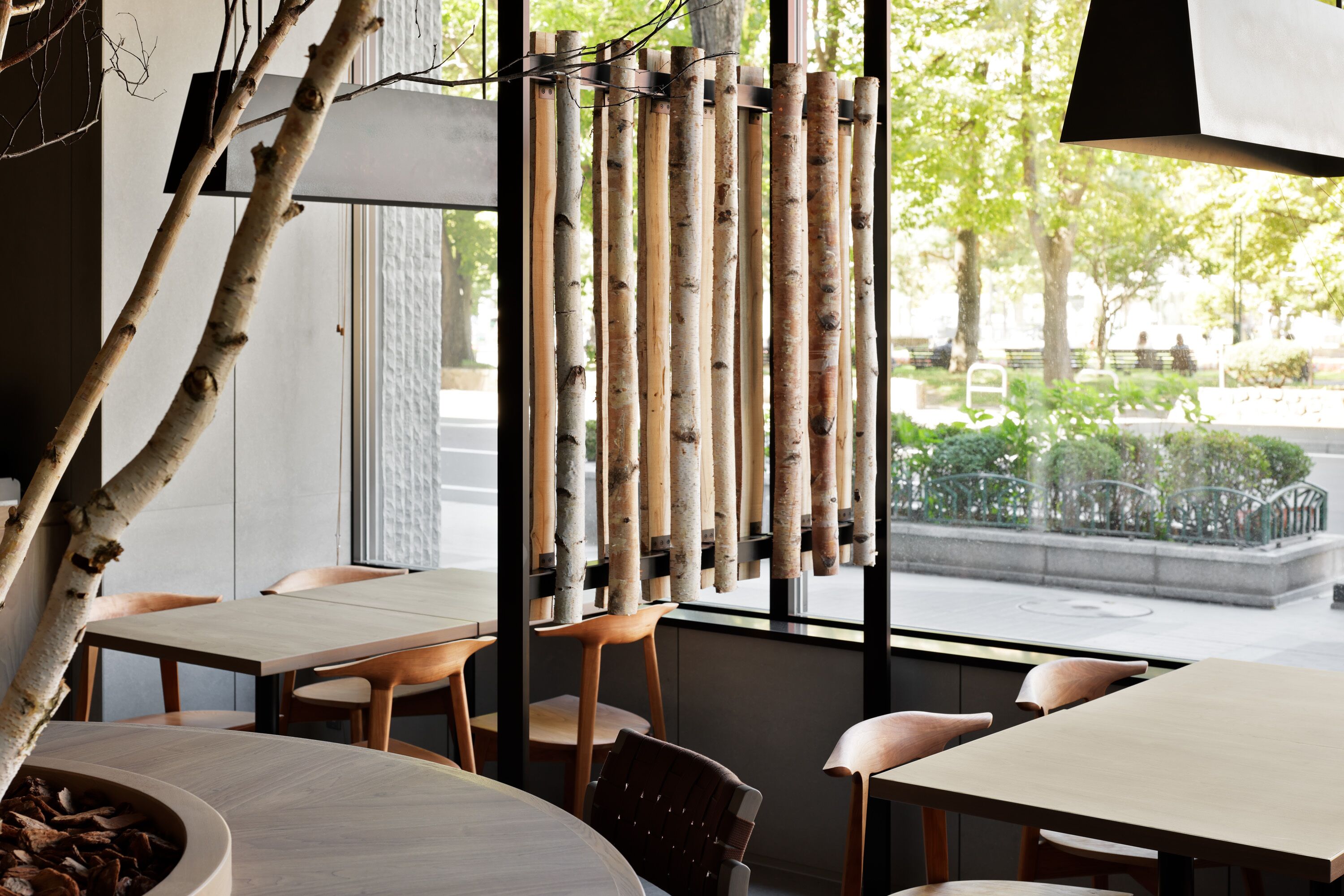 A restaurant with wooden tables and chairs, a bamboo screen, and a view of the street outside.