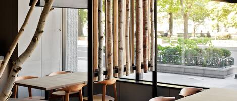 Un restaurante con mesas y sillas de madera, una pantalla de bambú y vistas a la calle.