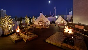 Una terraza en la azotea con dos tiendas de campaña, asientos de madera y un hogar para la chimenea.