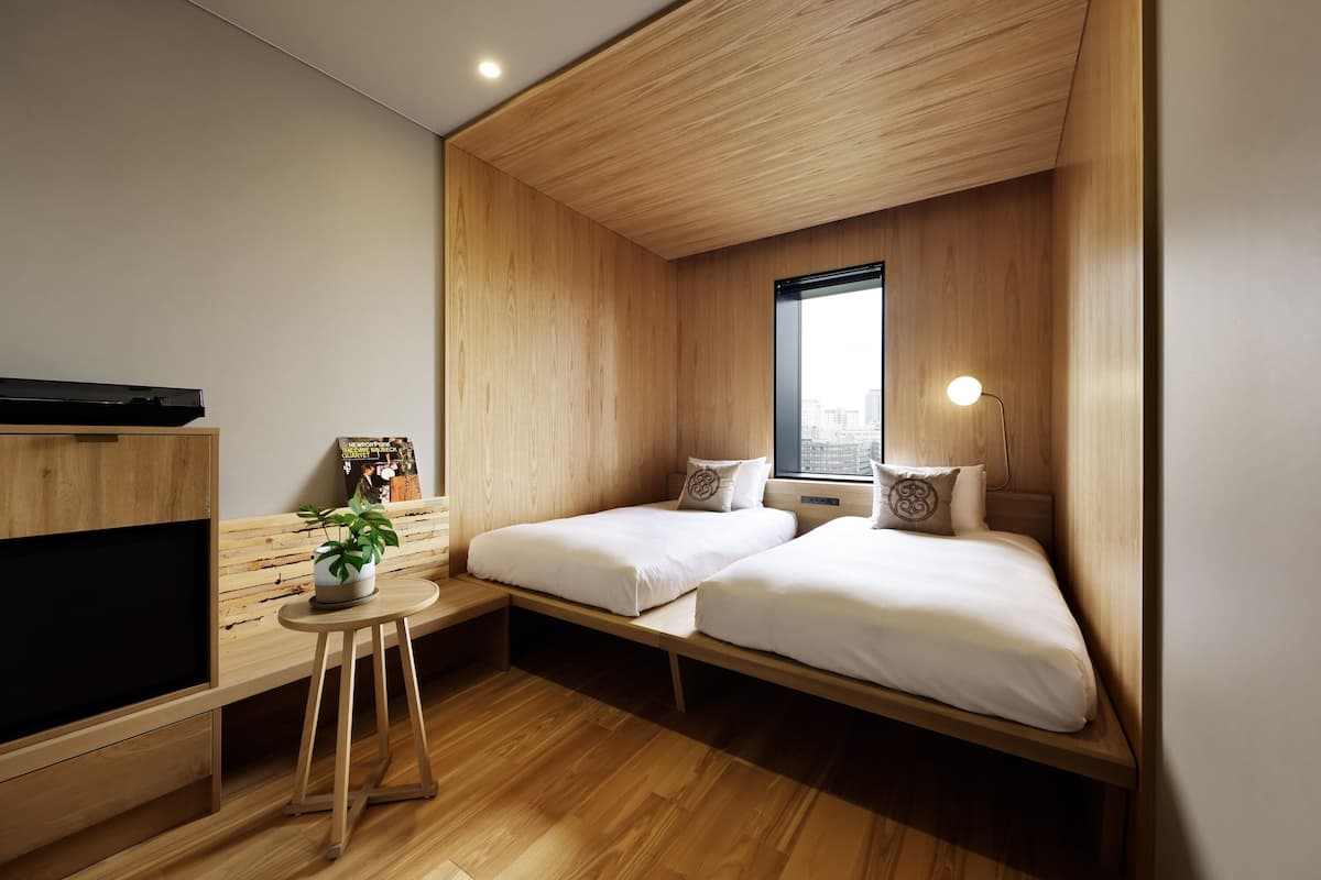 Una habitación moderna con dos camas, un escritorio, un televisor y una ventana con vista a la ciudad.