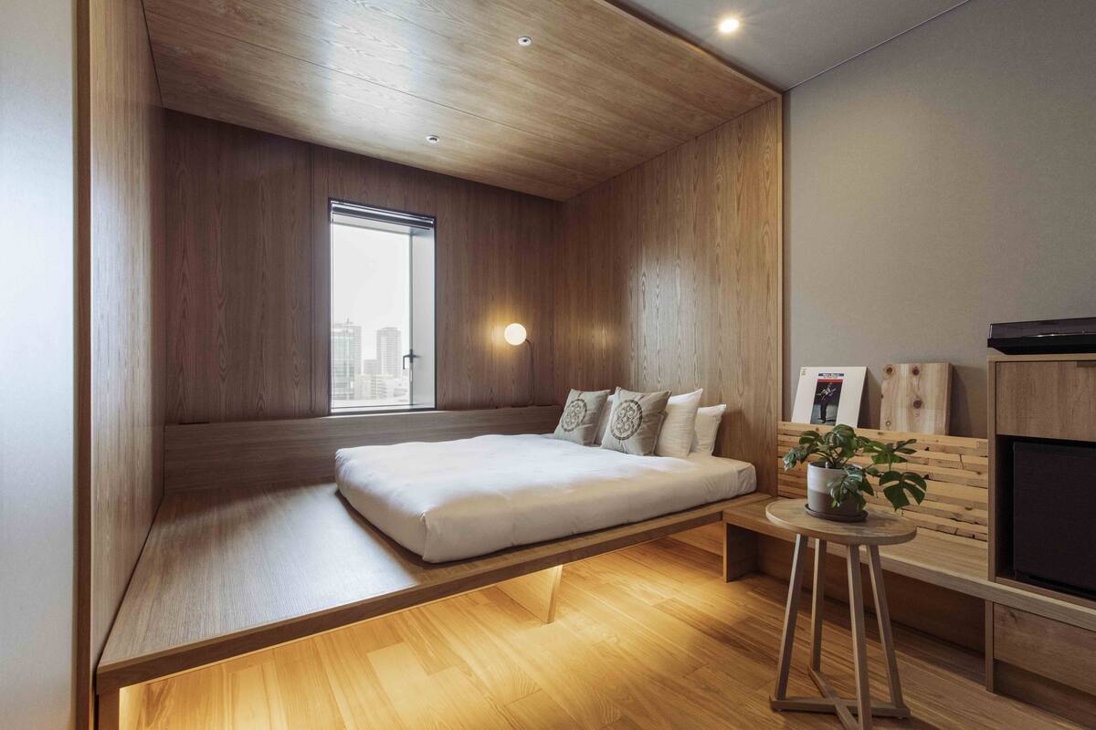 Un dormitorio moderno con cama empotrada, una mesita de noche pequeña, una planta en maceta y un televisor.