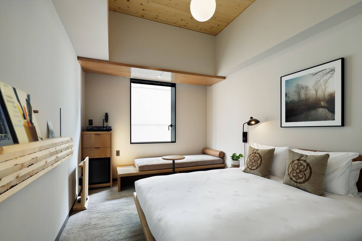 Un dormitorio moderno con una cama grande, un banco, una mesita y una ventana.