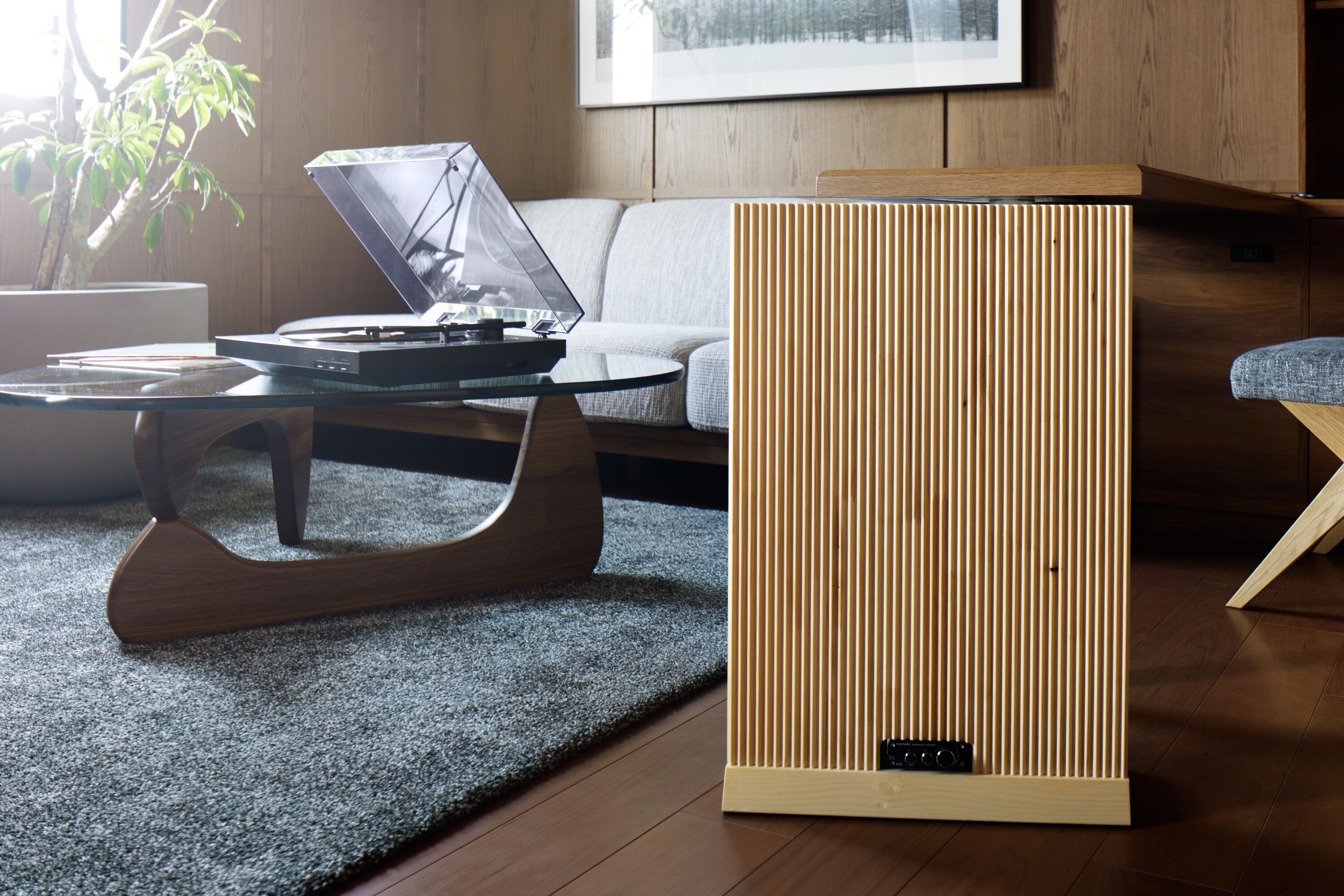 A modern living room with a glass coffee table, a wooden side table, a sofa, and a tall, vertical wooden panel.