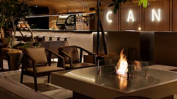A modern bar area with a glass-top table, chairs, and a visible fire feature.