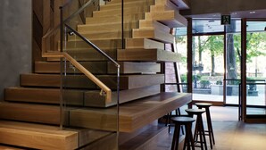 Una escalera moderna con barandillas de vidrio y escalones de madera, que conduce a un espacio exterior con asientos.