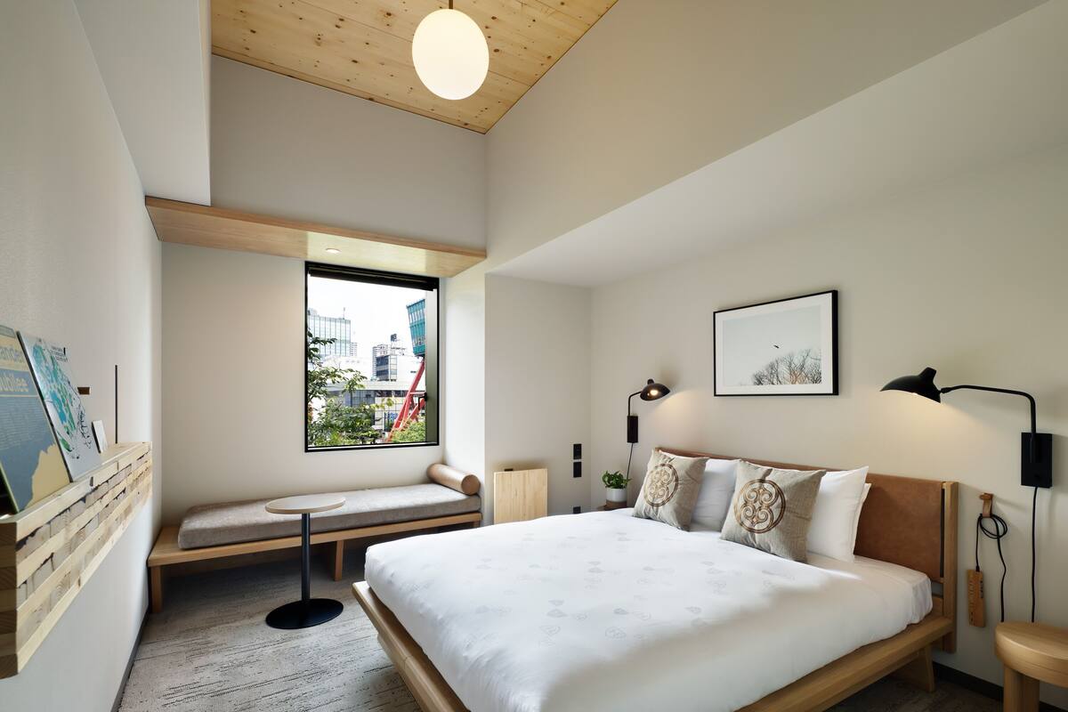 Un dormitorio moderno con una cama grande, un banco, una mesita y una ventana con vistas a la ciudad.