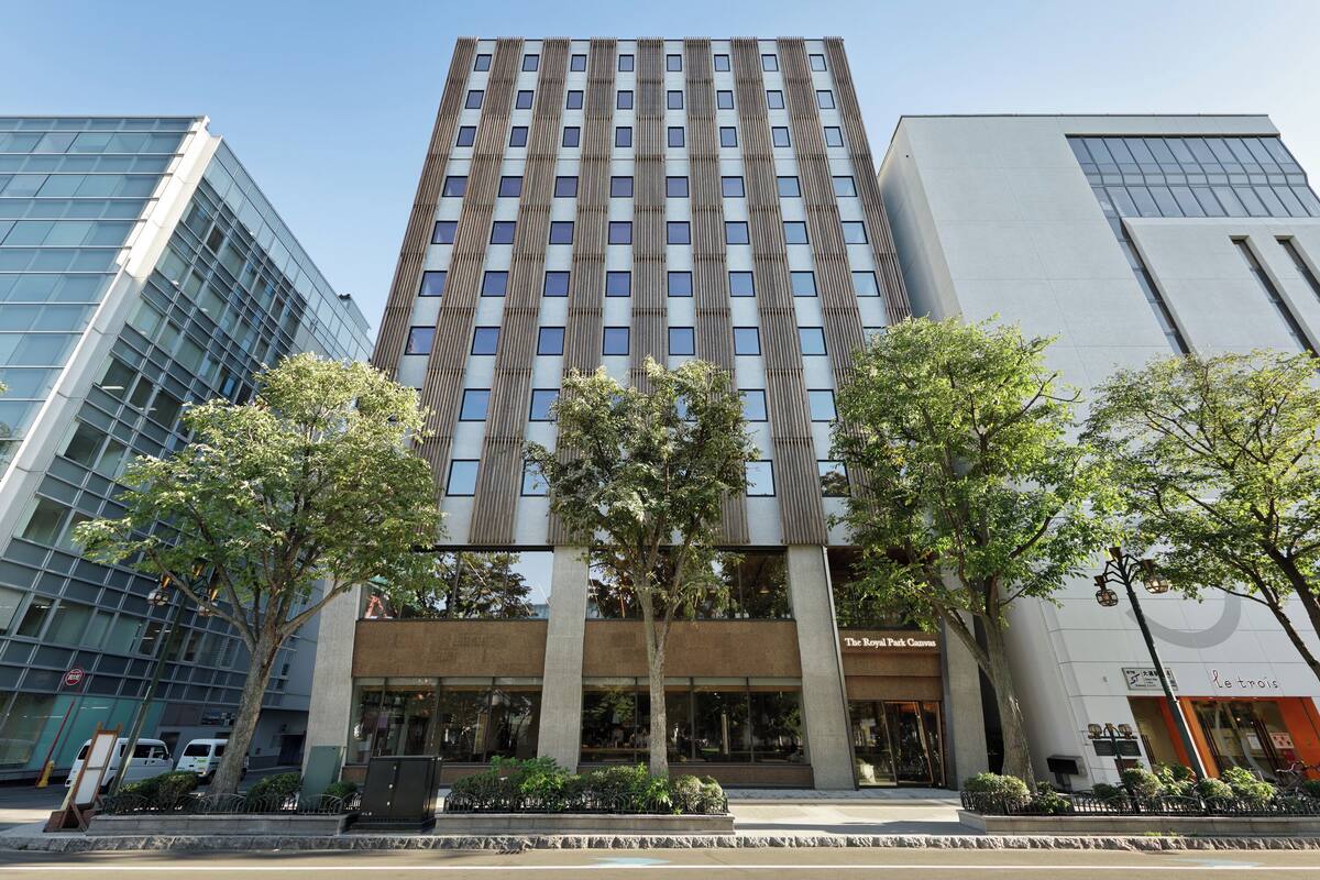 Un edificio moderno con fachada de vidrio, una entrada central y árboles en la parte frontal.