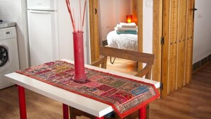 Una cocina con un refrigerador blanco, una lavadora, una silla de madera y una mesa con un florero rojo.