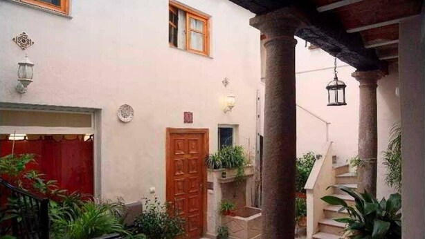 Un patio con puerta roja, una escalera y plantas en macetas.