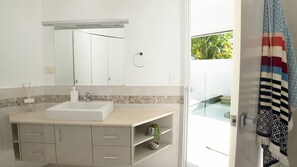 A modern bathroom with a large mirror, a sink, and a shower area visible through an open door.