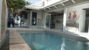 A swimming pool with clear water, surrounded by a modern house with large windows and a glass door.