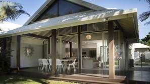 A modern house with a covered patio, large windows, and a dining area with white chairs. - Nikatara - Mission Beach (Mission Beach)