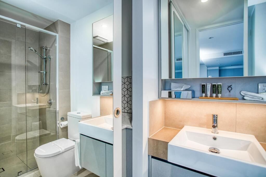 Un baño moderno con ducha de vidrio, inodoro y dos lavamanos con espejos.