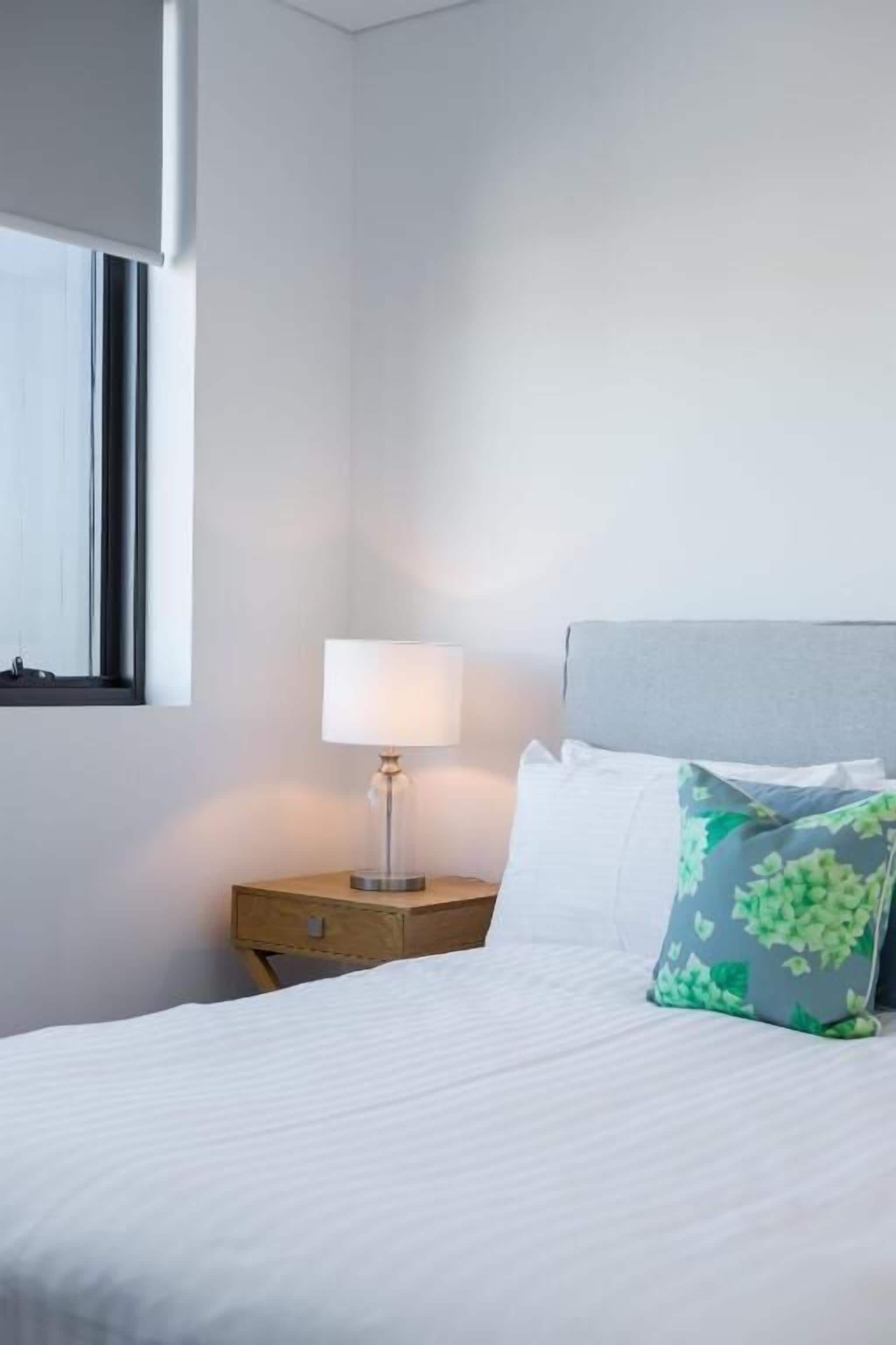 A neatly made bed with white bedding, a bedside lamp, and a floral pillow.