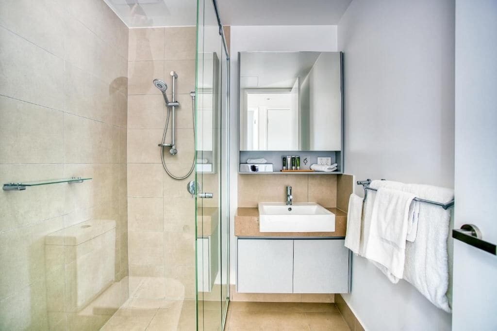 Une salle de bain moderne avec une douche à parois de verre, un lavabo blanc et un miroir au-dessus du lavabo.