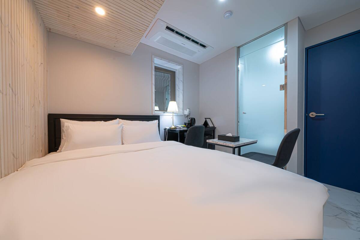 A hotel room with a large bed, a desk, a chair, and a blue door.
