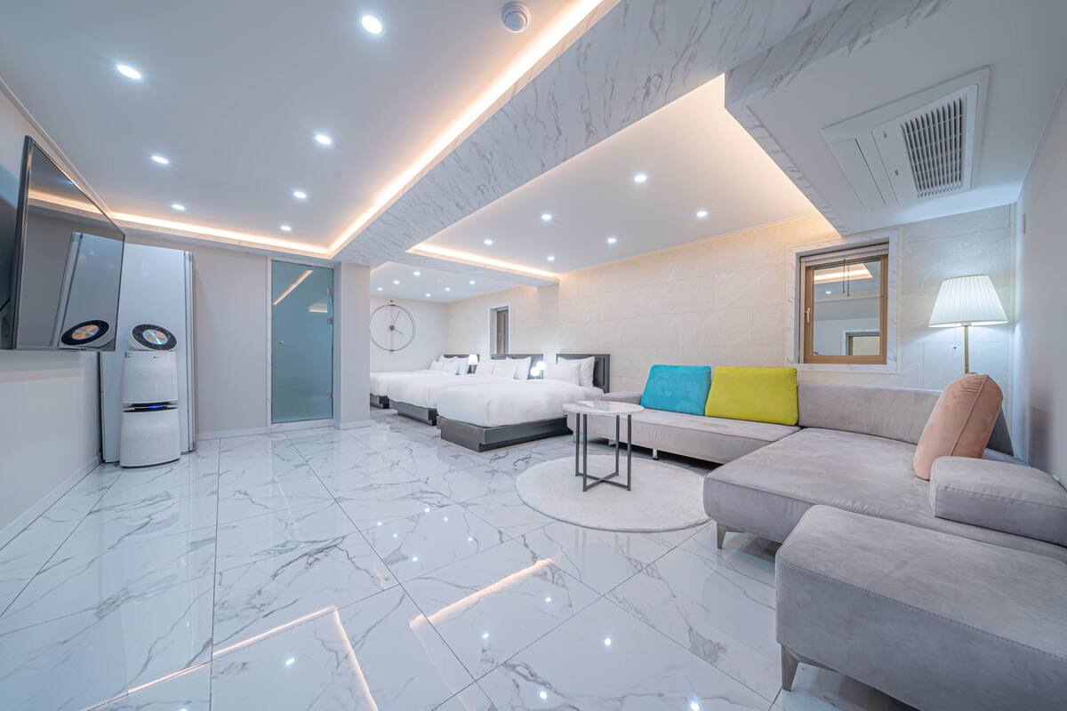 A modern hotel room with a large bed, a sofa, a small table, and a mirror.