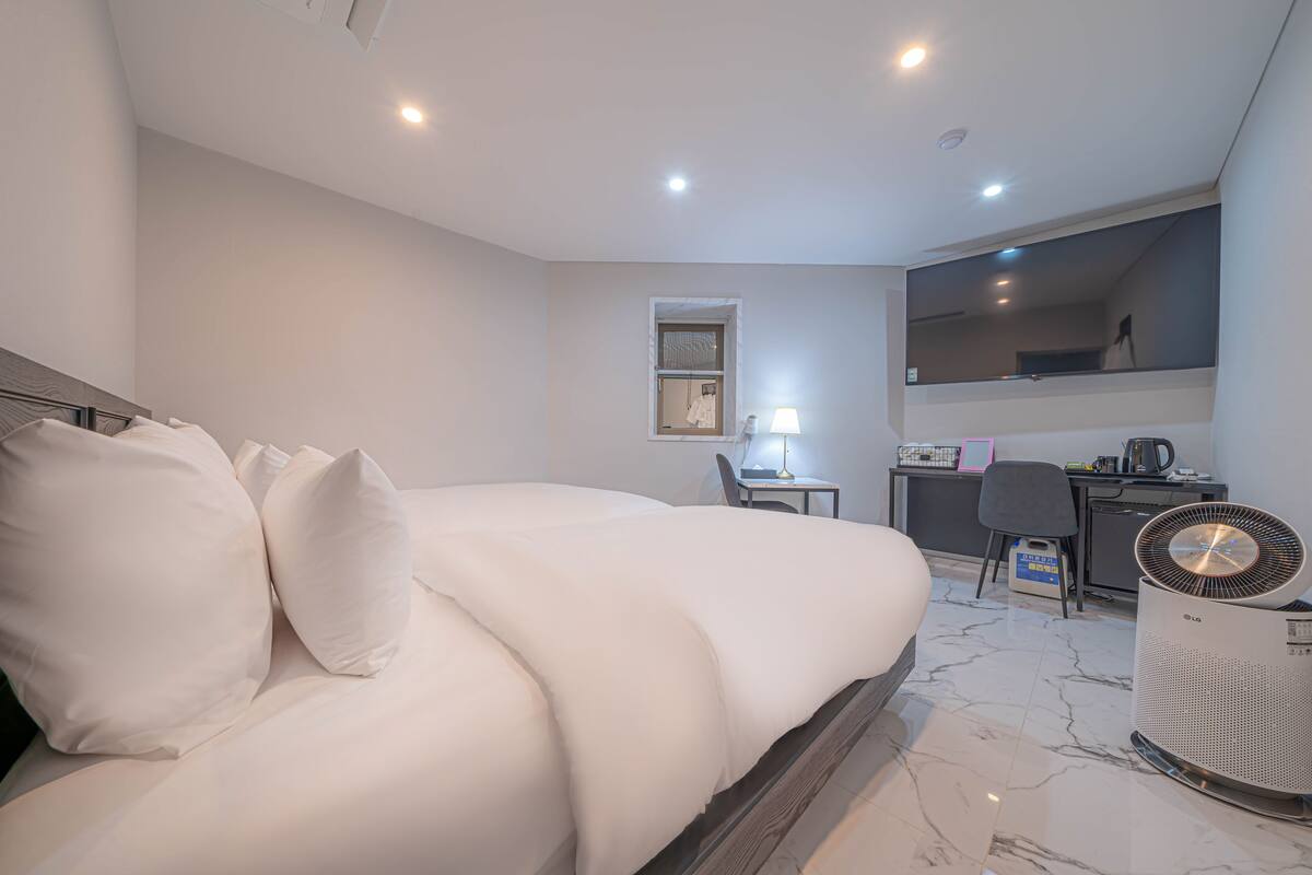 A modern hotel room with a large bed, a desk, a chair, a mirror, and a standing heater.