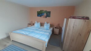 A bedroom with a bed, bedside tables, a nightstand, a wardrobe, and a wall-mounted picture.