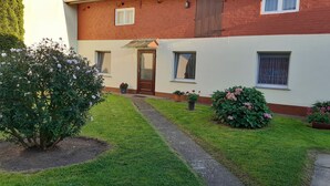 A residential building with a brick facade, a front door, and a small garden with a pathway leading to the entrance.
